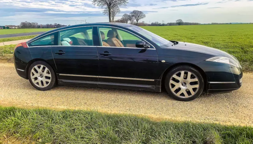 Ciemny Citroën C6 z beżowym wnętrzem stoi na żwirowej drodze obok zielonego pola.