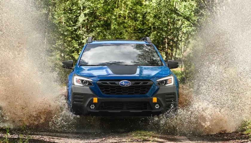 Niebieski Subaru Outback Wilderness z impetem wjeżdża w kałużę, tworząc fontannę wody i błota.