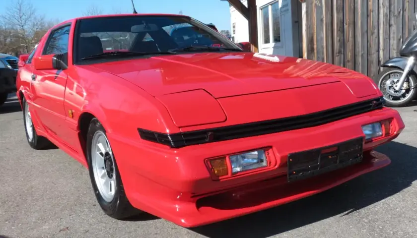 Czerwony Mitsubishi Starion z lat 80. błyszczy w słońcu. Klasyk sportowy z wysuwanymi światłami.