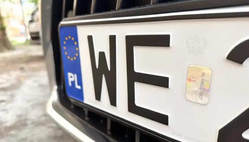 Zbliżenie na polską tablicę rejestracyjną z literami "WE". Widoczny symbol Unii Europejskiej i hologram.