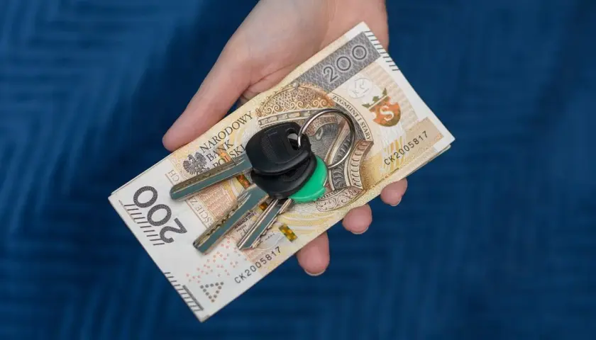 Dłoń trzyma banknot 200 zł i klucze. Symbolizuje to zsl rejestracja, np. kupno samochodu.