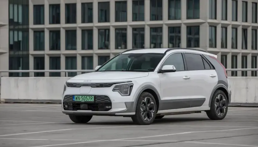 Białe Kia Niro stoi na parkingu przed nowoczesnym budynkiem. Sprawdź kia niro wymiary, by poznać jego gabaryty.