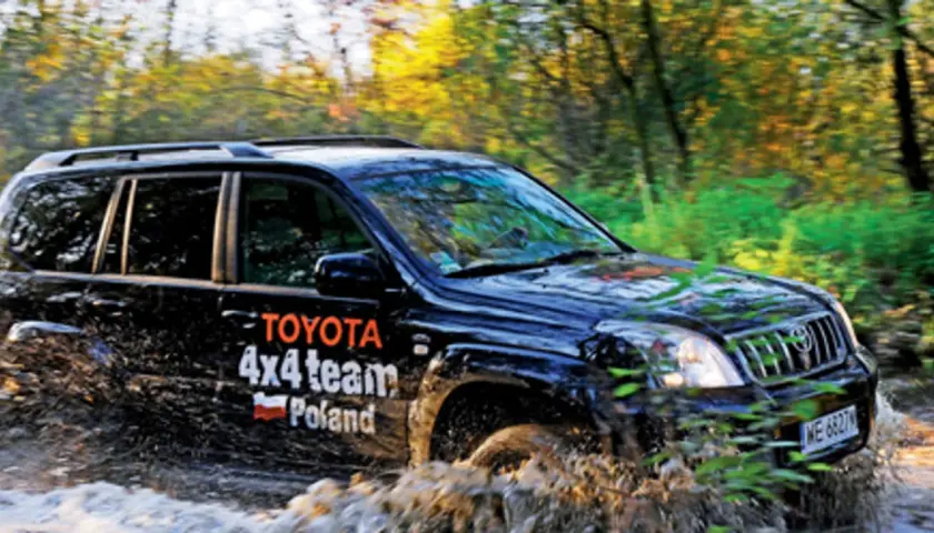 Czarny Toyota Land Cruiser 100 z napisem "4x4 team Poland" pokonuje błotnistą trasę w lesie.