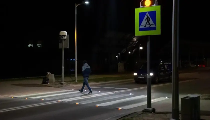 Nocą pieszy przechodzi przez pasy, oświetlone odblaskami. Obok miga żółte światło sygnalizatora, a znak d6 przypomina o obowiązku ustąpienia pierwszeństwa.