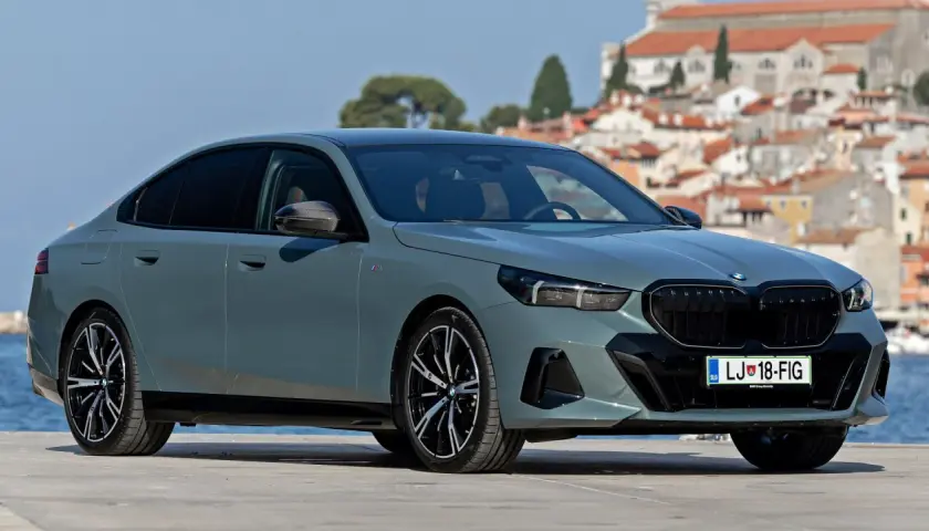 Eleganckie, szare BMW 520 z czarnymi felgami stoi na tle malowniczego, nadmorskiego miasteczka.