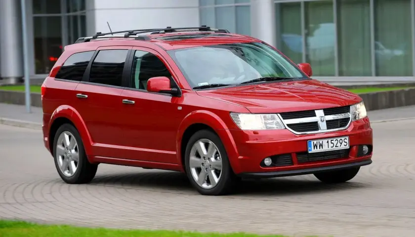 Czerwony Dodge Journey 3.6 z relingami dachowymi jedzie po brukowanej drodze.