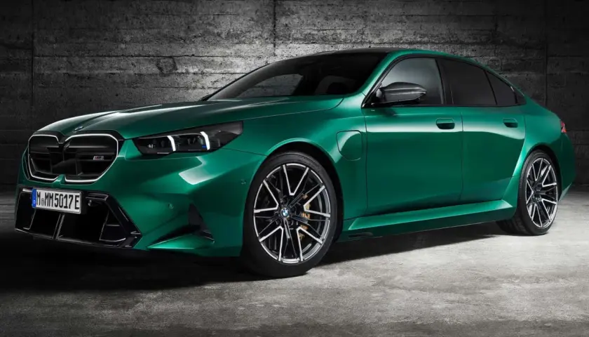Zielony BMW M5 Competition z nowoczesnymi światłami i felgami stoi na tle betonowej ściany.