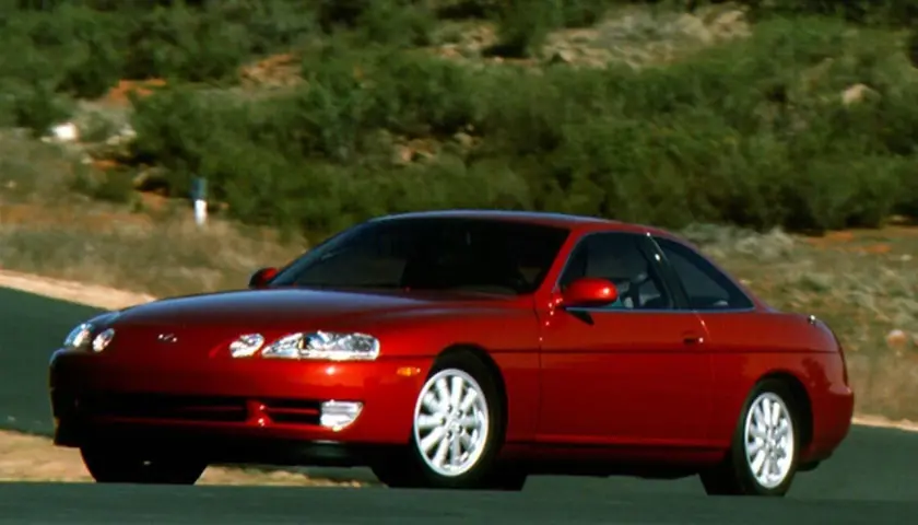 Czerwony Lexus SC400 na krętej drodze, otoczony zielonymi wzgórzami. Klasyczny sportowy samochód w ruchu.