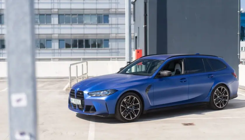 Niebieskie BMW G81 na parkingu, z nowoczesnym budynkiem w tle.