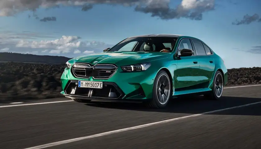 Zielony BMW M5 na drodze, chmury na niebie. Sprawdź aktualną bmw m5 cena i możliwości tego sportowego sedana.