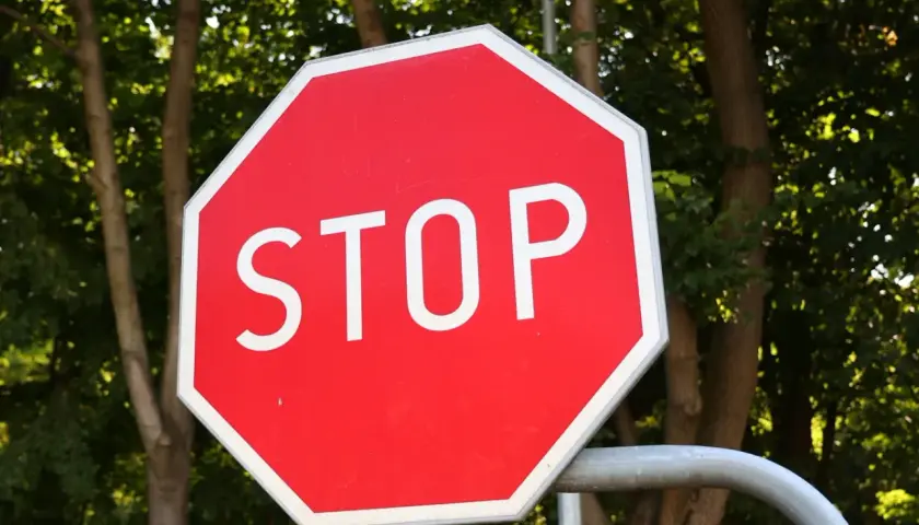 Ośmiokątny czerwony znak stop z białym napisem "STOP" na tle zielonych drzew.