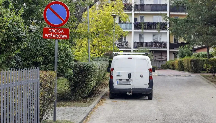 Znak "zakaz zatrzymywania się" na drodze pożarowej. Biały Fiat Doblò zaparkowany obok. Uważaj, bo grozi mandat za parkowanie.