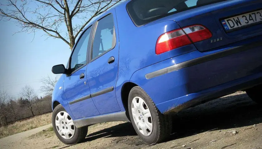 Niebieski Fiat Albea na tle drzew i błękitnego nieba.