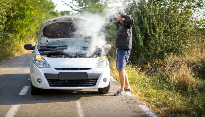 Mężczyzna z rozpaczą w rękach przy białym samochodzie, z którego bucha para. Rozbiegany diesel na poboczu drogi.