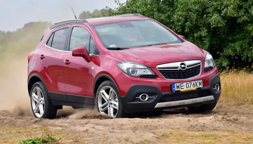Czerwony Opel Mokka 1.4 Turbo z napędem na cztery koła pokonuje piaszczysty teren, wzbijając tumany kurzu.
