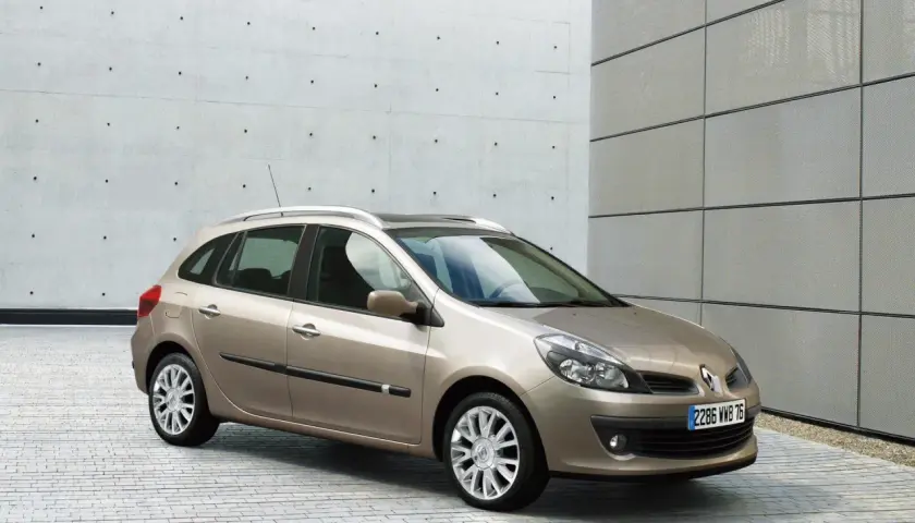 Beżowe Clio 3 kombi stoi na tle nowoczesnego budynku z betonową i metalową elewacją.