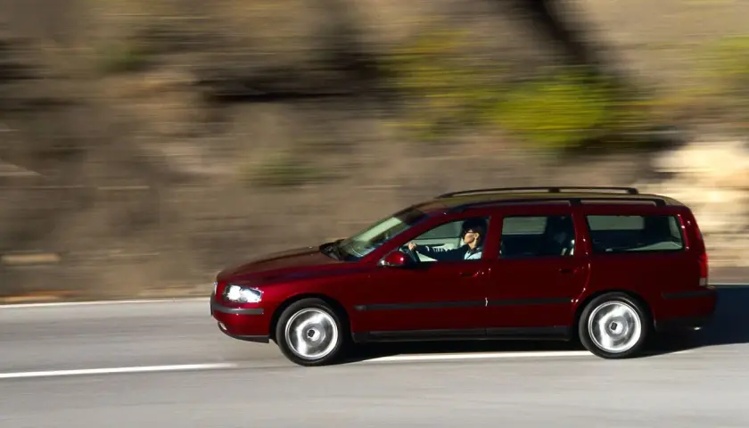 Czerwone volvo v70 ii jedzie po drodze, za kierownicą siedzi kobieta. Rozmyte tło sugeruje ruch.