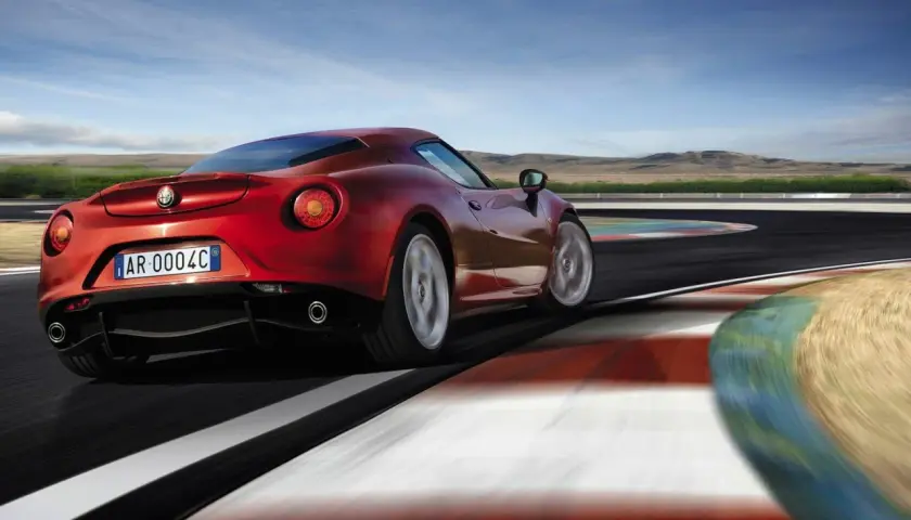 Czerwone Alfa Romeo 4C na torze wyścigowym, z rozmytymi kołami i kolorowymi bandami.