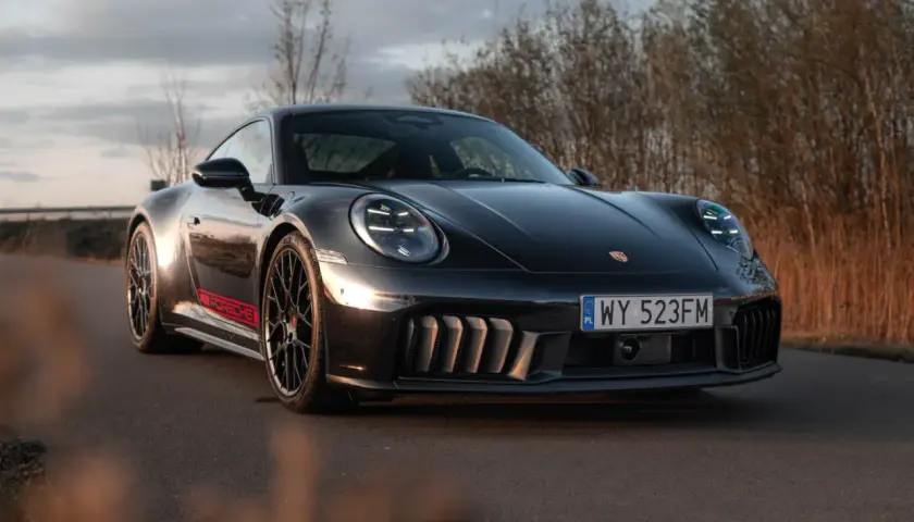 Czarny Porsche GTS z czerwonymi akcentami na progu, zaparkowany na drodze wśród suchych traw.