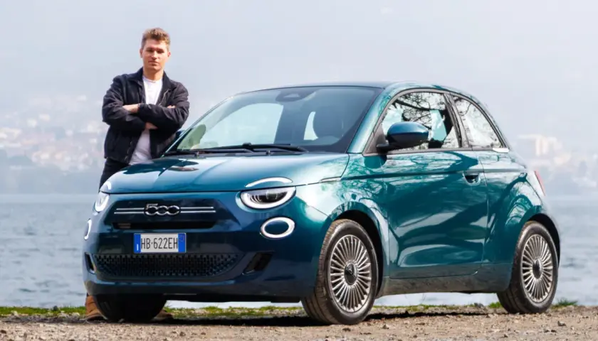 Młody mężczyzna stoi obok swojego nowego, turkusowego fiat mini 500 nad jeziorem.