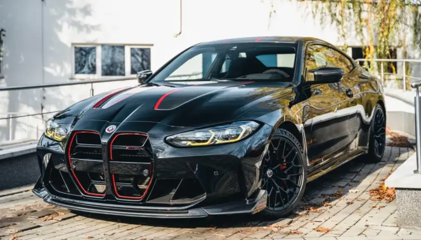 Czarny BMW M4 CSL z czerwonymi akcentami i sportowym dyfuzorem, zaparkowany na bruku.