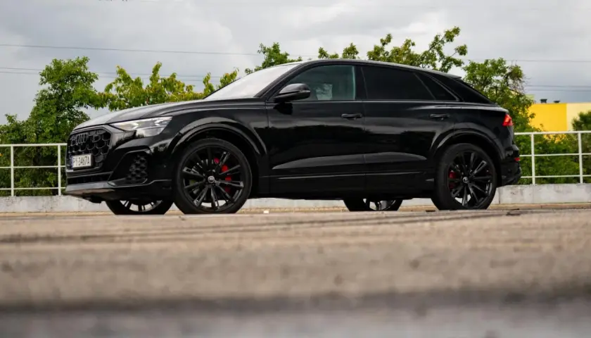Czarny Audi Q9 z czerwonymi zaciskami hamulcowymi, odbijający się w kałuży. Sprawdź audi q9 cena!
