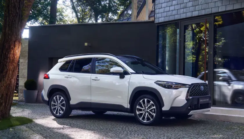 Biała Toyota Corolla Cross zaparkowana przed nowoczesnym budynkiem. Sprawdź jej wymiary, by poznać jej kompaktową sylwetkę.