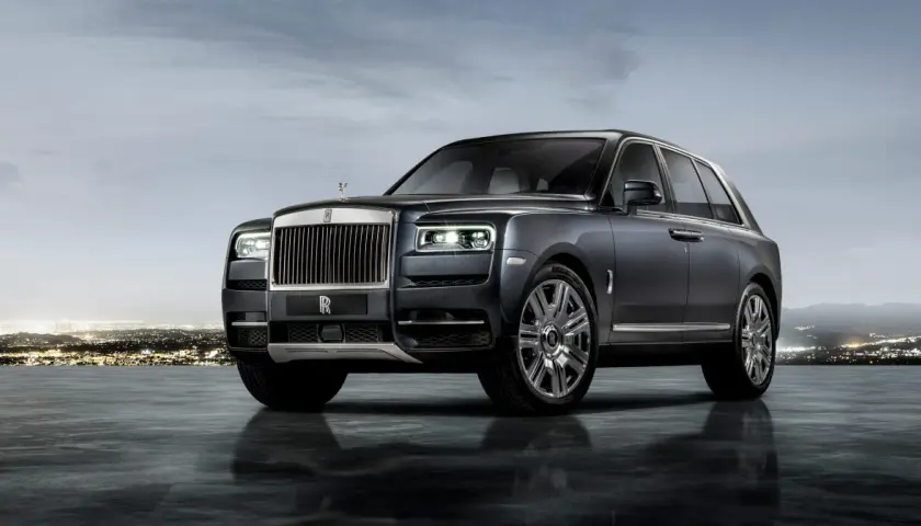 Elegancki Rolls-Royce SUV w ciemnym kolorze, lśniącym na tle nocnego miasta i gór.