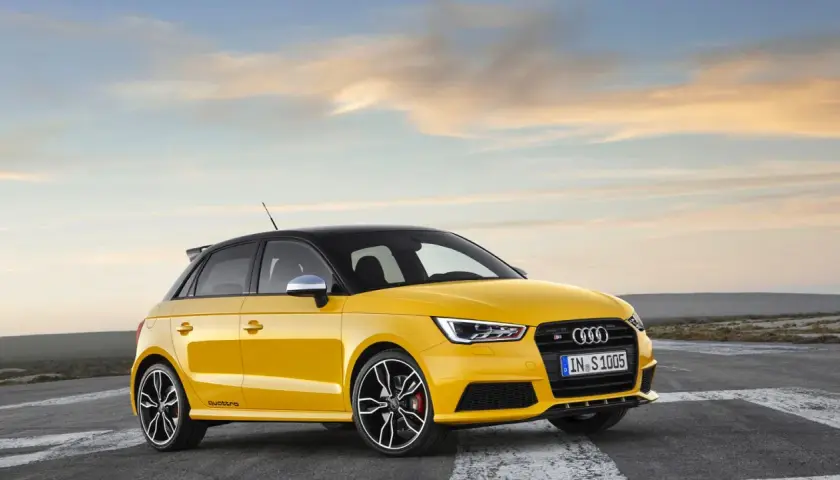Żółty Audi RS1 z czarnym dachem i felgami, gotowy do jazdy po pustej drodze o zachodzie słońca.