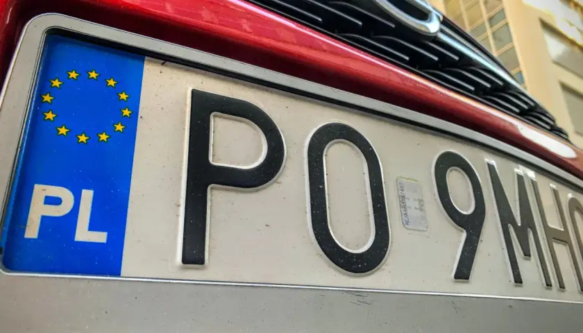Czerwony samochód z polską tablicą rejestracyjną PO 9MH0. Widoczny fragment grilla i logo marki.