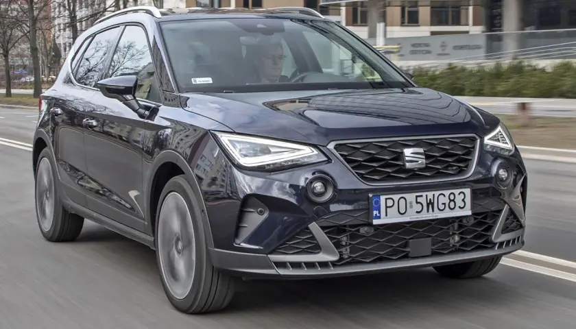 Ciemnogranatowy Seat Arona FR jedzie ulicą. Kierowca w okularach prowadzi auto.