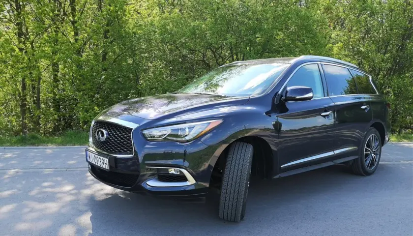 Ciemny Infiniti QX60 zaparkowany na poboczu drogi, otoczony zielenią drzew.
