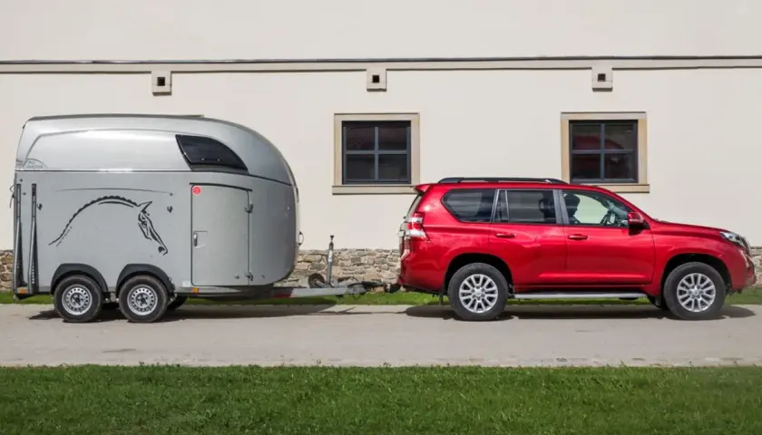 Czerwony SUV holuje przyczepę kempingową z rysunkiem konia. Idealny zestaw dla posiadaczy prawa jazdy na przyczepę.