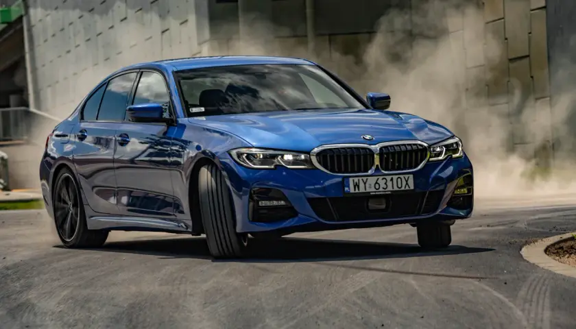 Niebieskie BMW 330i G20 w zakręcie, unosząc tumany kurzu.