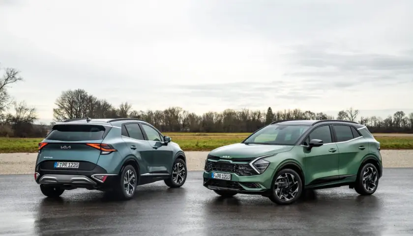 Dwa nowe Kia Sportage GT Line w zielonych odcieniach stoją na mokrej drodze.