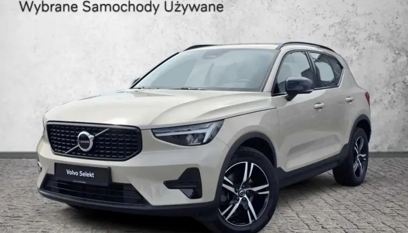 Jasny beżowy Volvo XC40, używane z salonu, prezentuje się elegancko na tle betonowej ściany.