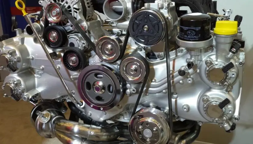 Błyszczący silnik Subaru z paskami, kołami pasowymi i filtrem oleju. Widać tu wiele elementów, w tym jeden duży cylinder.