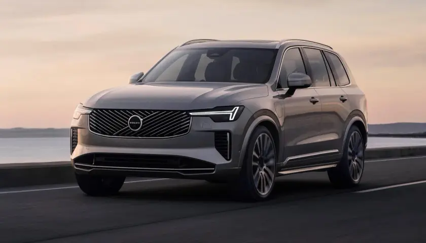 Elegancki, szary Volvo CX90 jedzie po drodze nad morzem o zachodzie słońca.