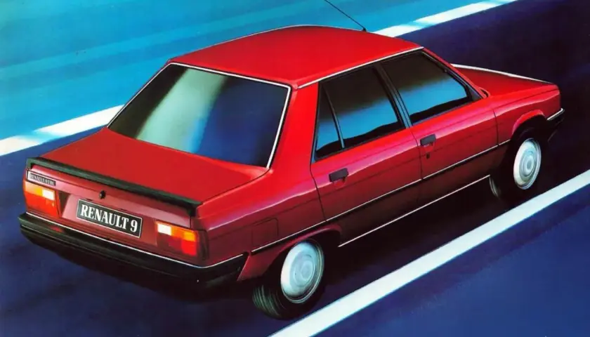 Czerwony Renault 9 sunie po drodze, odbijając niebieskie niebo w szybach.
