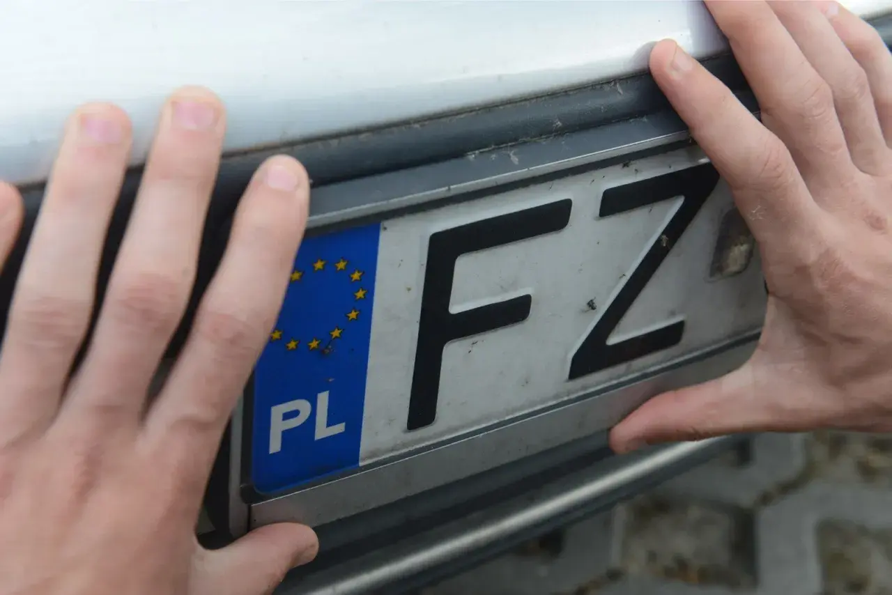 Dłonie trzymają tablicę rejestracyjną z oznaczeniem "PL FZ". To ważny element rejestracji pojazdu.