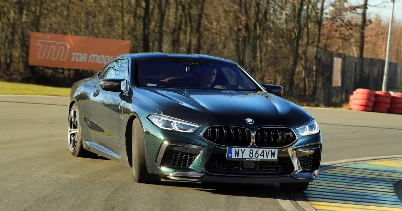Mocne m8 bmw w ciemnozielonym kolorze na torze wyścigowym, z widocznym banerem "TOR MODLIN" w tle.