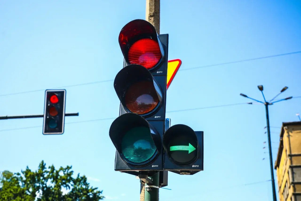 Sygnalizator S2 z zieloną strzałką w prawo i czerwonym światłem na głównym słupku. Niebo błękitne.