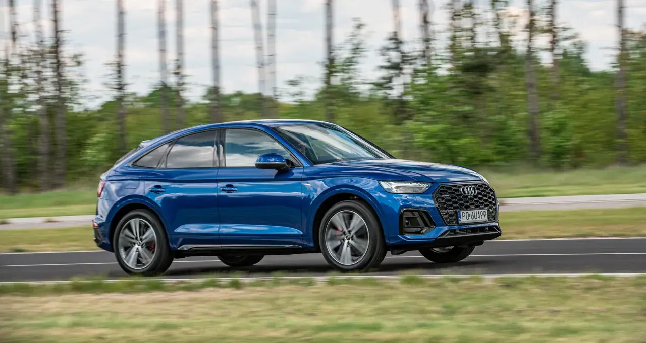 Błękitny Audi Q5 Sportback 2025 w ruchu, z rozmytym tłem lasu. Dynamiczna sylwetka i sportowy charakter.