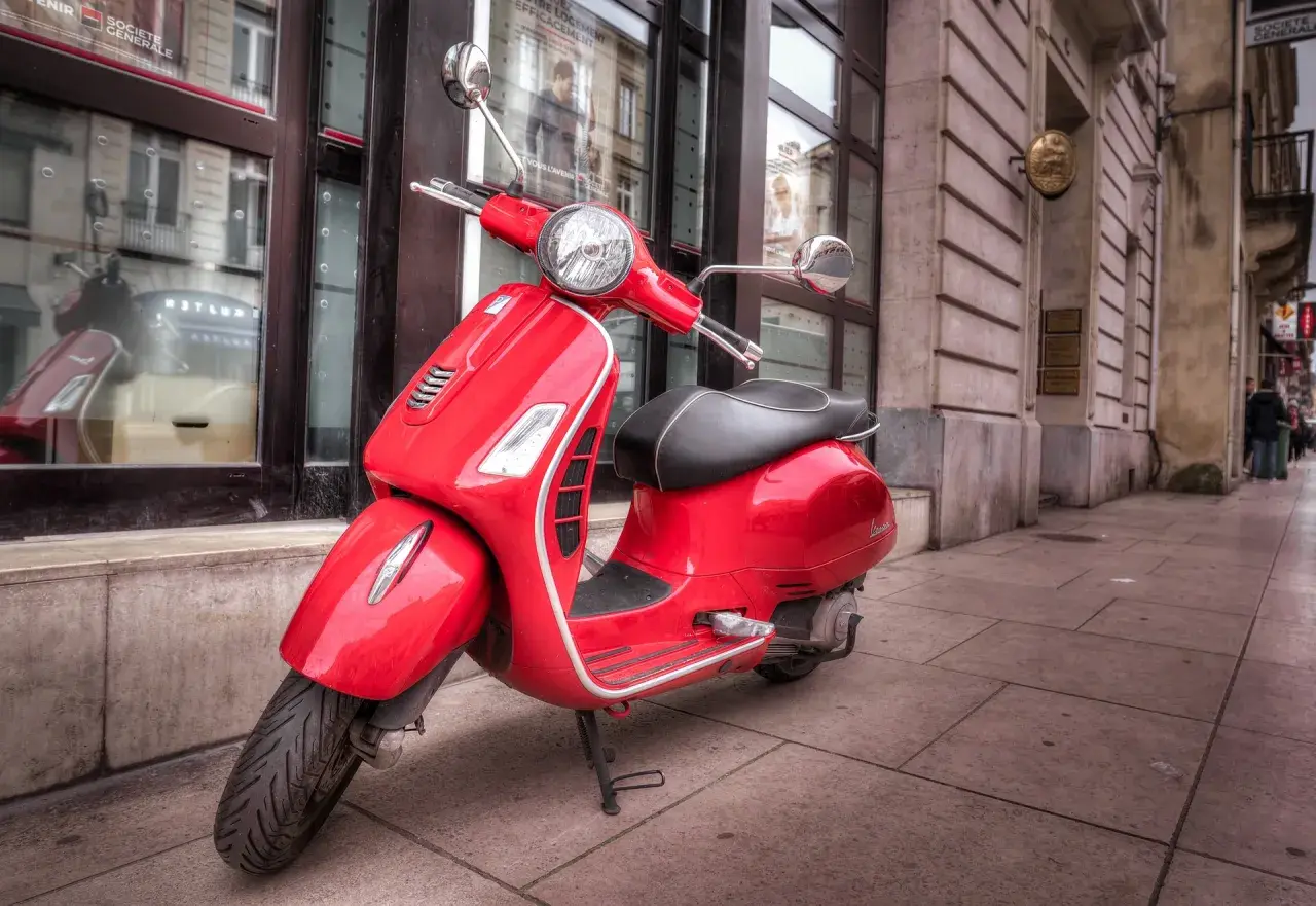 Czerwona Vespa, idealna do miejskiej kategoria am czym można jeździć. Stylowy pojazd na brukowanym chodniku.
