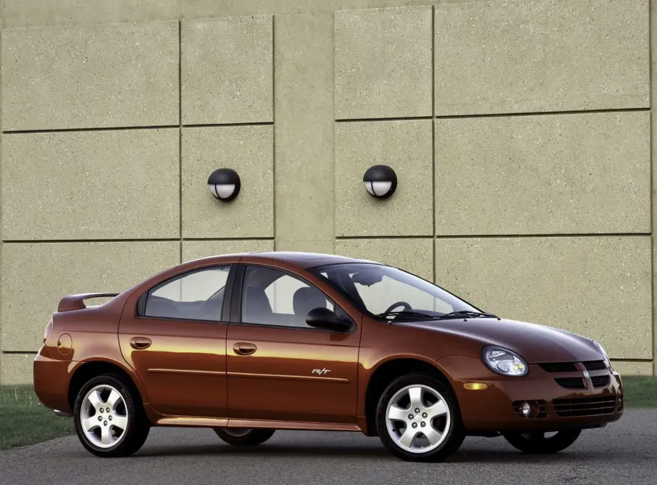 Brązowy Dodge Neon R/T z 2004 roku stoi przed betonową ścianą z dwoma okrągłymi lampami.