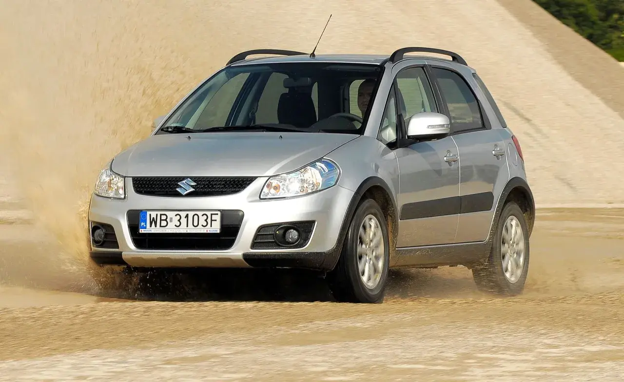 Srebrny Suzuki SX4 1.6 benzyna pokonuje piaszczystą wydmę, wzbijając tumany piasku.