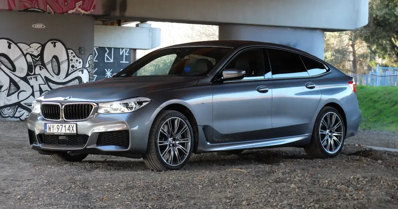 Eleganckie bmw 640d w szarym kolorze zaparkowane pod mostem z graffiti.