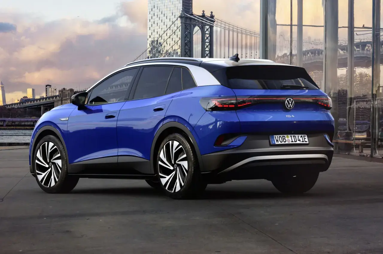 Niebieski Volkswagen ID.4 z białym dachem, zaparkowany na tle miasta z mostem i nowoczesnymi budynkami.