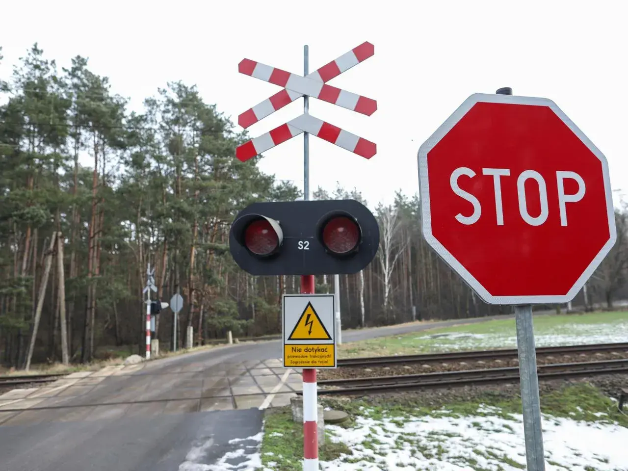 Przejazd kolejowy bez zapór z czerwonym światłem i znakiem STOP. Uważaj na tory!
