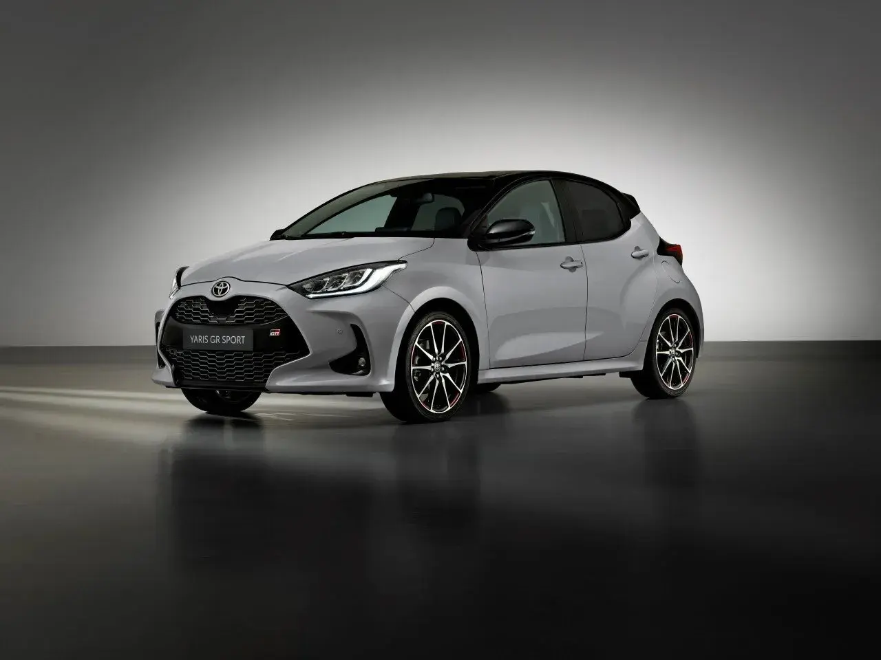 Srebrny Toyota Yaris GR Sport z czarnym dachem i sportowymi felgami stoi na ciemnej podłodze.